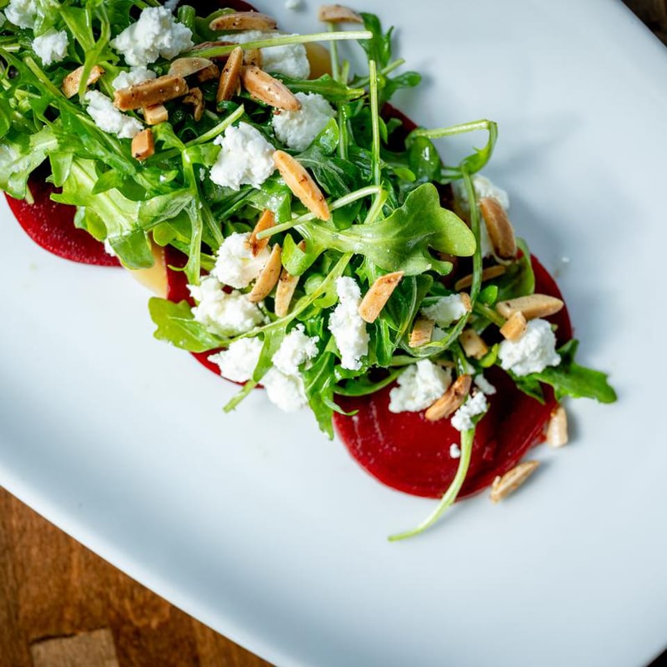 Beet salad with arugula, goat cheese, and sliced almonds on a white plate.