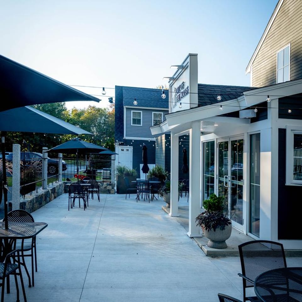 Outdoor patio dining area with black tables, chairs, umbrellas, and string lights at dusk.