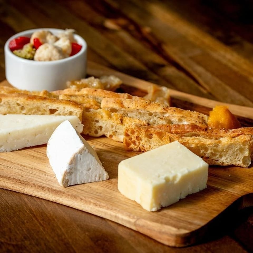 Cheese board with assorted cheeses, sliced rustic bread, fruit, and nuts arranged on a wooden serving board.