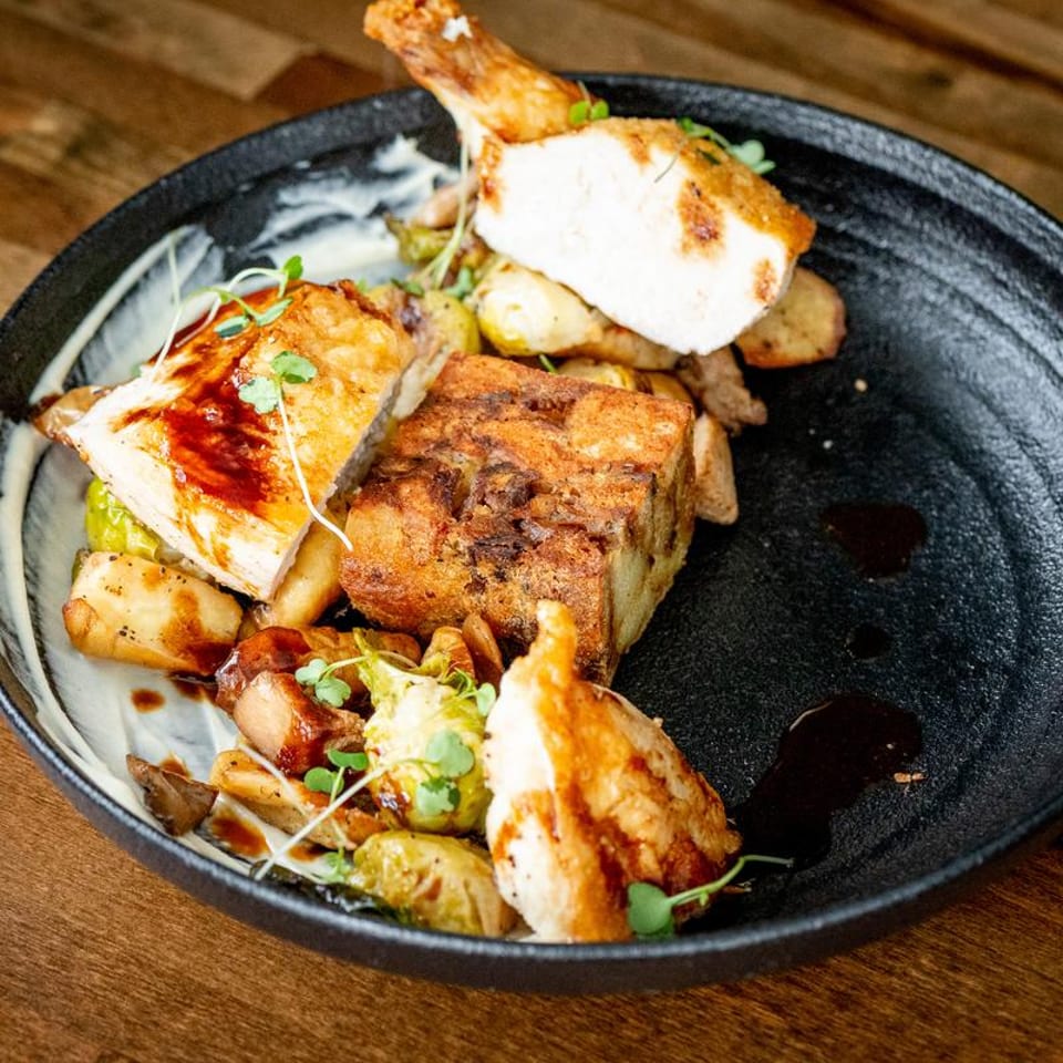 Roasted chicken pieces, a large potato gratin, and brussels sprouts on a black plate.