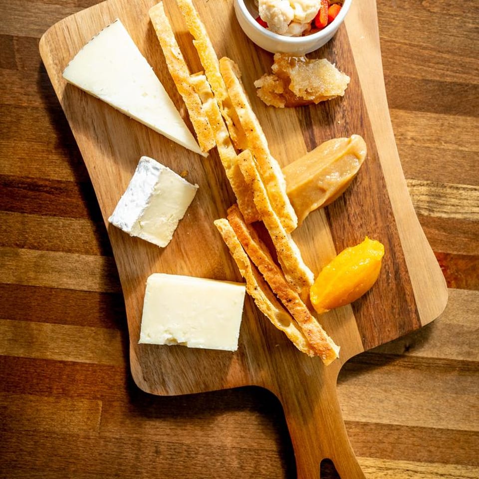 Cheese board with various cheeses, breadsticks, honeycomb, and fruit paste on a wooden surface.
